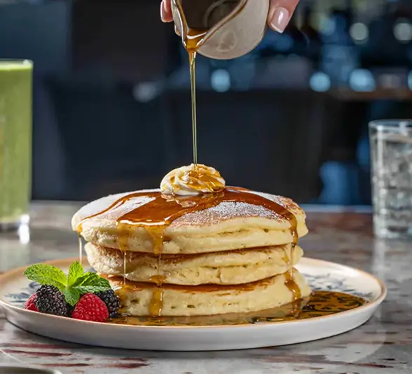 Stack of fluffy pancakes topped with butter and drizzled with syrup, served with fresh berries.