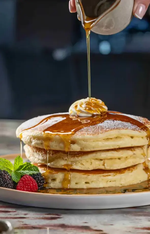Stack of fluffy pancakes topped with butter and drizzled with syrup, served with fresh berries.