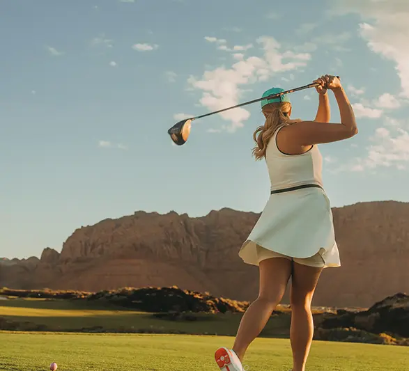Woman teeing off on a golf course with desert mountains in the background.