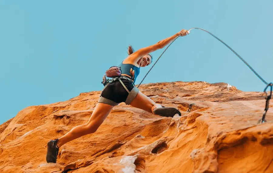 Woman rock climbing on a red sandstone cliff in a desert landscape.